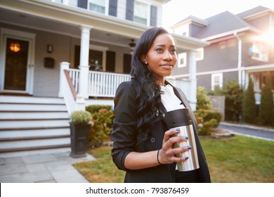 Businesswoman With Cup Of Coffee Leaving Suburban House For Work