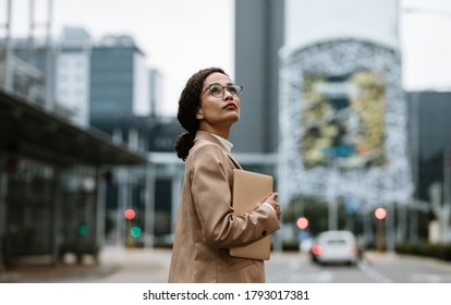 Businesswoman With A Digital Tablet Looking Up Over Her Shoulder. Female Business Professional Looking Back At Her Office Building.