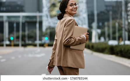 Businesswoman with a digital tablet walking on city street looking back at camera and smiling. Female business professional going home after work.