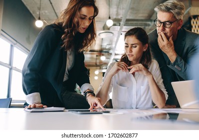 Businesswoman discussing new strategies with her team sitting around a table. Group of business people having a meeting on new project in office. - Shutterstock ID 1702602877