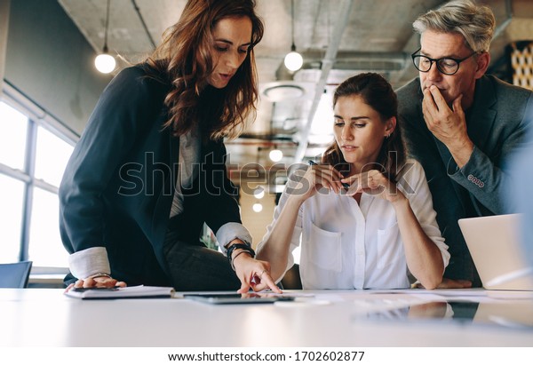 Businesswoman discussing new strategies with her\
team sitting around a table. Group of business people having a\
meeting on new project in\
office.