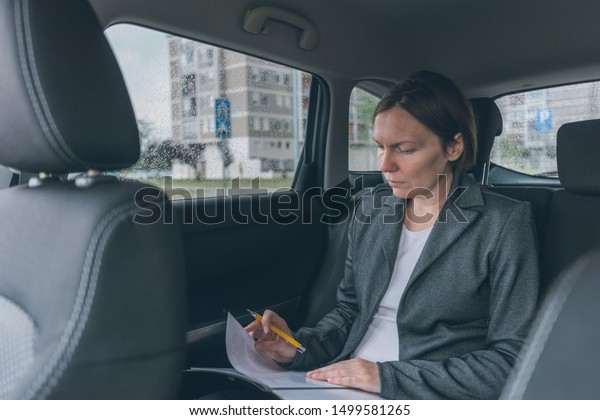 Businesswoman doing business paperwork on\
car back seat, adult caucasian female businessperson executive\
analyzing business results while traveling by\
automobile