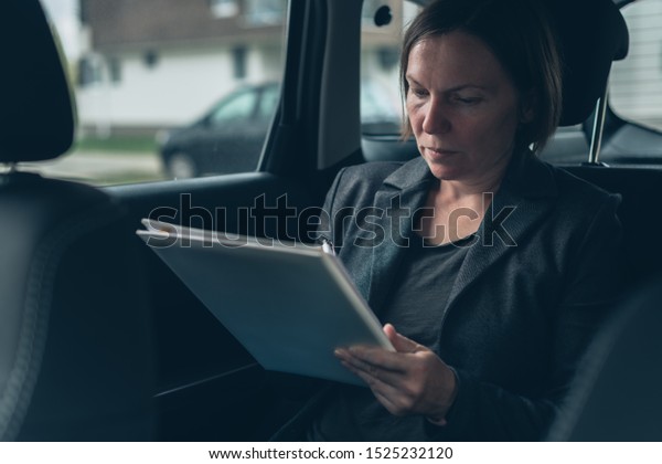 Businesswoman doing paperwork and\
analyzing business report while sitting in car at the back\
seat