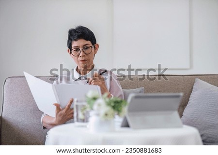 Businesswoman doing paperwork sitting with tablet on sofa in living room at home