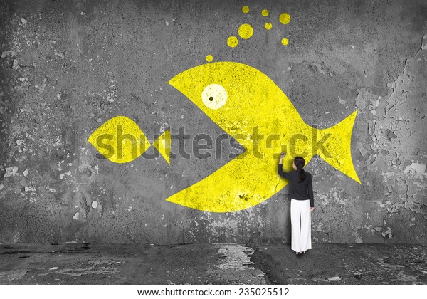 businesswoman drawing  big fish eat small fish on\
the wall