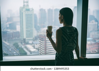 Businesswoman Drinking Coffee At Work Contemplative Looking Out The Window Of High Rise Skyscraper Building During Morning Tea Break. Stress, Mental Health In The Workplace. Career Job Concept.