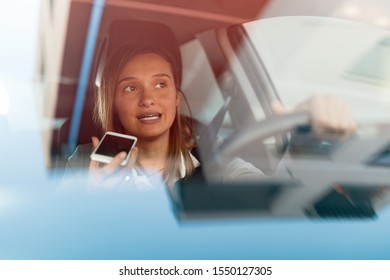 Businesswoman Driving To Work And Talking On Cell Phone Behind The Wheel. The View Is Through The Glass. 