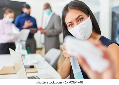 Businesswoman with everyday mask disinfecting computer in the office because of Covid-19 and corona virus