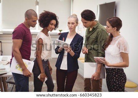 Businesswoman explaining to creative team while holding tablet computer at office
