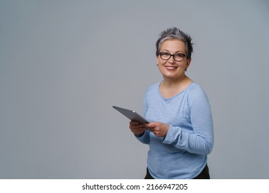 Businesswoman In Eye Glasses And Digital Tablet In Hands Working Online Smile Looking At Camera. Pretty Woman In 50s In Blue Blouse Isolated On White. Older People And Technologies.