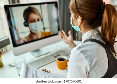 Businesswoman with face mask communicating with her colleague via video call while working in the office during COVID-19 pandemic.  - Powered by Shutterstock