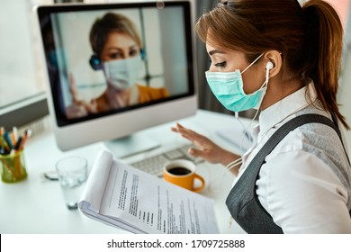 Businesswoman with face mask going through reports while having online meeting with her colleague in the office.  - Powered by Shutterstock