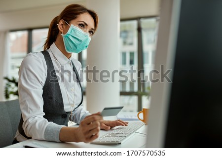 Businesswoman with face mask using computer and shopping on the internet with credit card in the office during COVID-19 pandemic. 