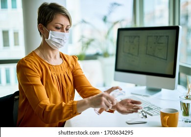 Businesswoman with face mask using hand sanitizer while cleaning her hands in the office.  - Powered by Shutterstock