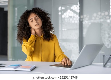 Businesswoman feeling neck pain sitting at desk using laptop. Expression shows workplace discomfort. Scene represents stress and strain in office settings. - Powered by Shutterstock