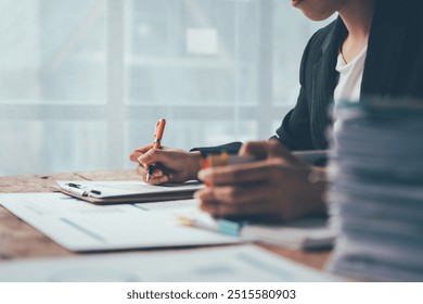 Businesswoman Focus: A young businesswoman intently writing on a clipboard, surrounded by stacks of documents, showcasing the dedication and focus required in the corporate world.   - Powered by Shutterstock