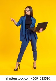 Businesswoman full-length portrait. Woman makes a pointing gesture. Businesswoman with laptop. Female executive on orange background. A girl in a pantsuit and heels. 
