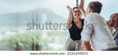 Photo of Businesswoman giving a high five to male colleague in meeting. Business professionals high five during a meeting in boardroom.