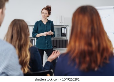 Businesswoman Giving A Presentation Or In House Training To A Group Of Young Professional People In An Office Viewed Between The Heads And Shoulders