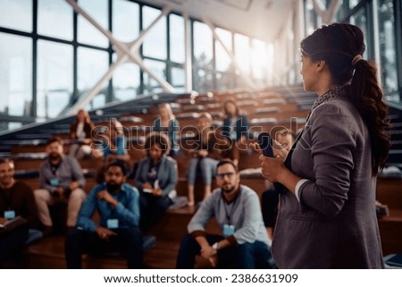 Businesswoman giving a speech to group of entrepreneurs during an education event at convention center.