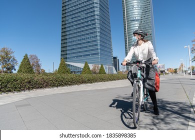 Businesswoman Going To Work At Office By Bicycle. Young Woman Wears A Surgical Mask. Concept On The Environment And More Sustainable Cities