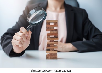 Businesswoman hand holding glass magnifying over wooden blocks tower. Business analysis, Risk Management, Study, opportunities and strategy Concepts