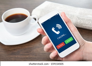 Businesswoman Hand Holding A Phone With Blue Screen And The Phone Ringing Tube Against The Background Of The Table In The Office