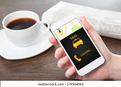 businesswoman hand holding a phone with interface taxi against the background of the table in the office