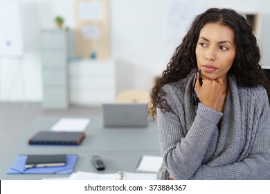 businesswoman with hand on chin sitting at desk in the office in thoughts - Powered by Shutterstock