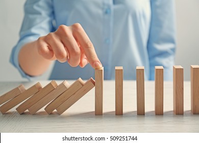 Businesswoman Hand Trying To Stop Toppling Dominoes On Table