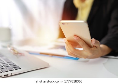 Businesswoman hands in black suit sitting and using mobile phone. Woman working or using computer on white table in modern office with notebook 