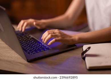 A businesswoman has a job in the office or works at home remotely, sits at the table, uses a copybook for writing notes and laptop for typing text on the keyboard. Close up with no face focused.
