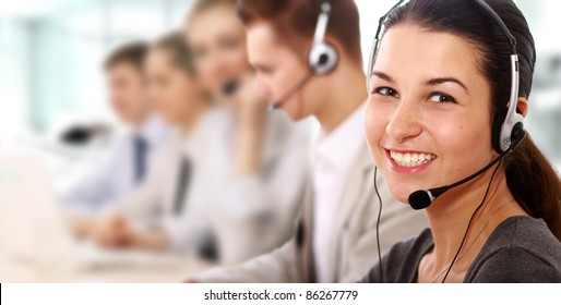 Businesswoman with headset smiling at  camera in call center. Businessmen in headsets on background