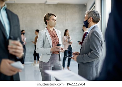 Businesswoman and her coworker wearing protective face masks and communicating after education event in a hallway of an office building. - Shutterstock ID 1961112904