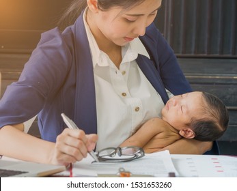 Businesswoman Holding Baby In Her Arms While Working, Signing Contract. Single Mom Taking Care Of Newborn In The Office. Mother's Love Concept.