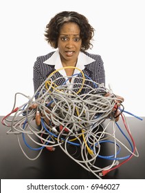 Businesswoman Holding Bundle Of Tangled Computer Cords With Overwhelmed Look On Her Face.