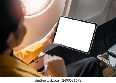 Businesswoman holding a digital tablet with a blank screen while seated on an airplane, ideal for work or entertainment during travel. - Powered by Shutterstock