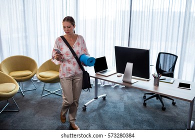 Businesswoman holding an exercise mat and looking her mobile phone in the office - Powered by Shutterstock