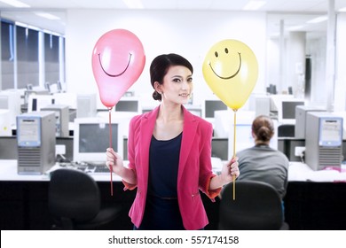 Businesswoman holding happy balloons with smiley face at office - Powered by Shutterstock