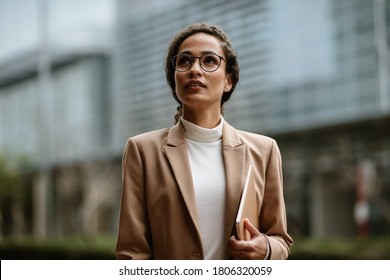 Businesswoman holding a laptop walking outdoors. Woman in formalwear and eyeglasses walking in the city. - Powered by Shutterstock