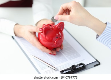 Businesswoman is holding a red piggy bank, client puts coin into it