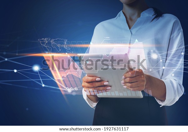 Businesswoman holding\
tablet and using technological approach to optimize business\
process. System hologram charts and graph flying nearby smartphone.\
Office on\
background.