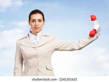 Businesswoman Holds Vintage Red Phone On Distance. Serious Operator In Business Suit Posing With Telephone On Blue Sky Background. Employee Ignores Communication. Business Assistance And Support.