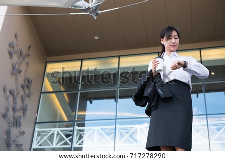 businesswoman in a hurry holding coffee looking at her watch outside office building. young woman with tea checking time while going to work outdoors. business people is late for work or a meeting.