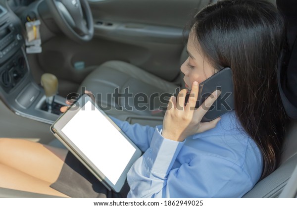 Businesswoman inside a car using a tablet and\
mobile phone for\
working.