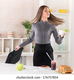 Businesswoman In The Kitchen Getting Ready For Work. She Is Rushing For Work. Holding A Bag With Laptop In One Hand And Coffee In Other. 