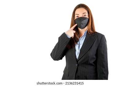 Businesswoman With KN95 FFP2 Black Mask Pointing It. Wearing A Suit, Looking At Camera. Isolated On White Background. 40-45 Years Old Woman.