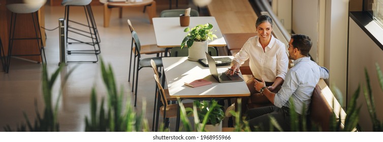 Businesswoman with laptop explaining project details to colleague at office desk. Business partners having meeting in coworking office space.