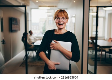 Businesswoman with a laptop laughing while working in an office with colleagues having a meeting in the background - Shutterstock ID 2116963904