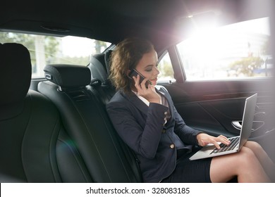 Businesswoman with laptop receiving a phone call on the backseat of a car. Female entrepreneur working during travelling to office in a luxury car. - Powered by Shutterstock